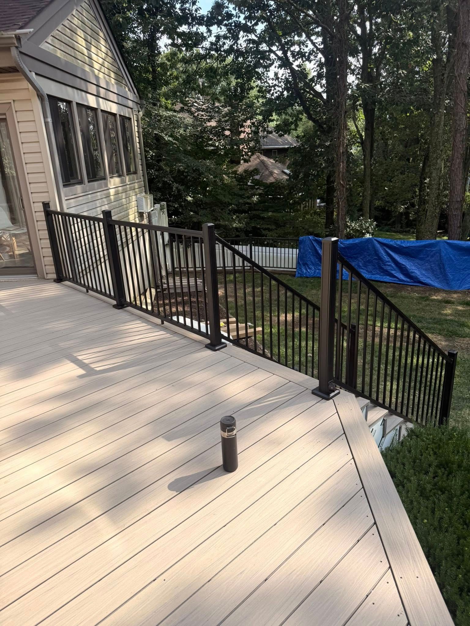Deck with black railing, brown posts, tan decking, and a sunroom in the background.
