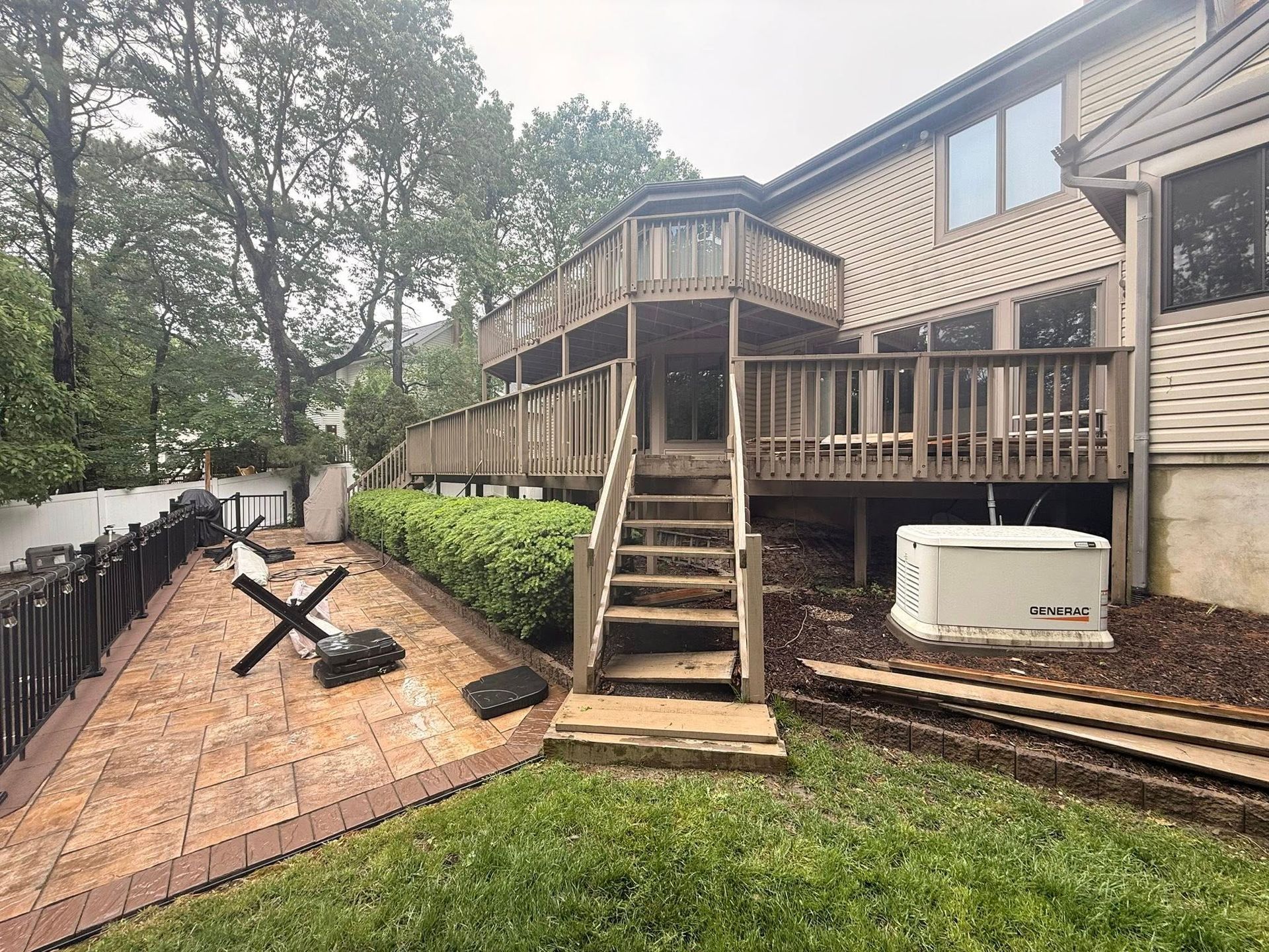 Backyard with multi-level wooden deck and steps leading down to a tiled patio area; a generator is next to the house.