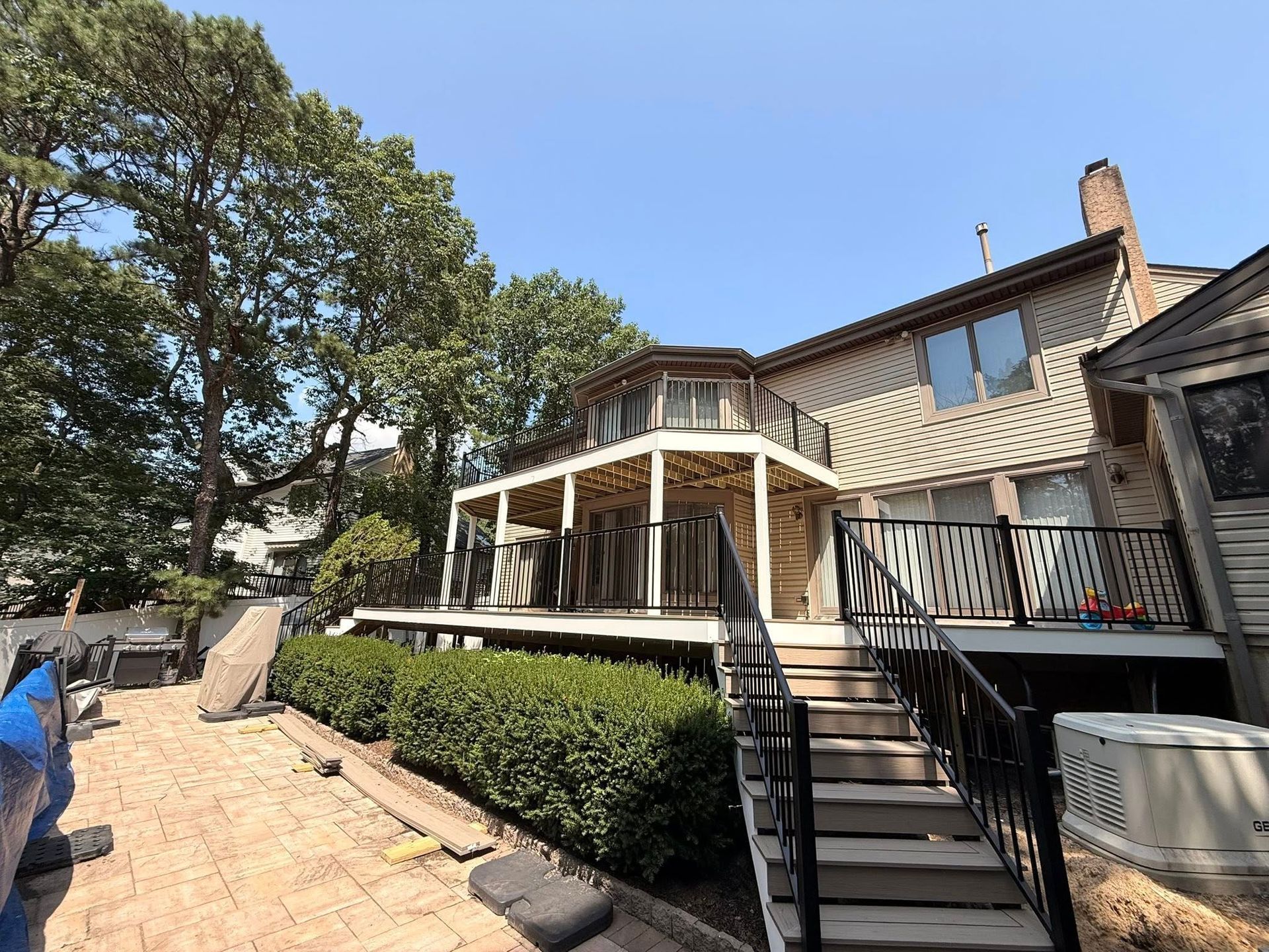 Two-story house with decks, stairs, and a hedge on a sunny day.