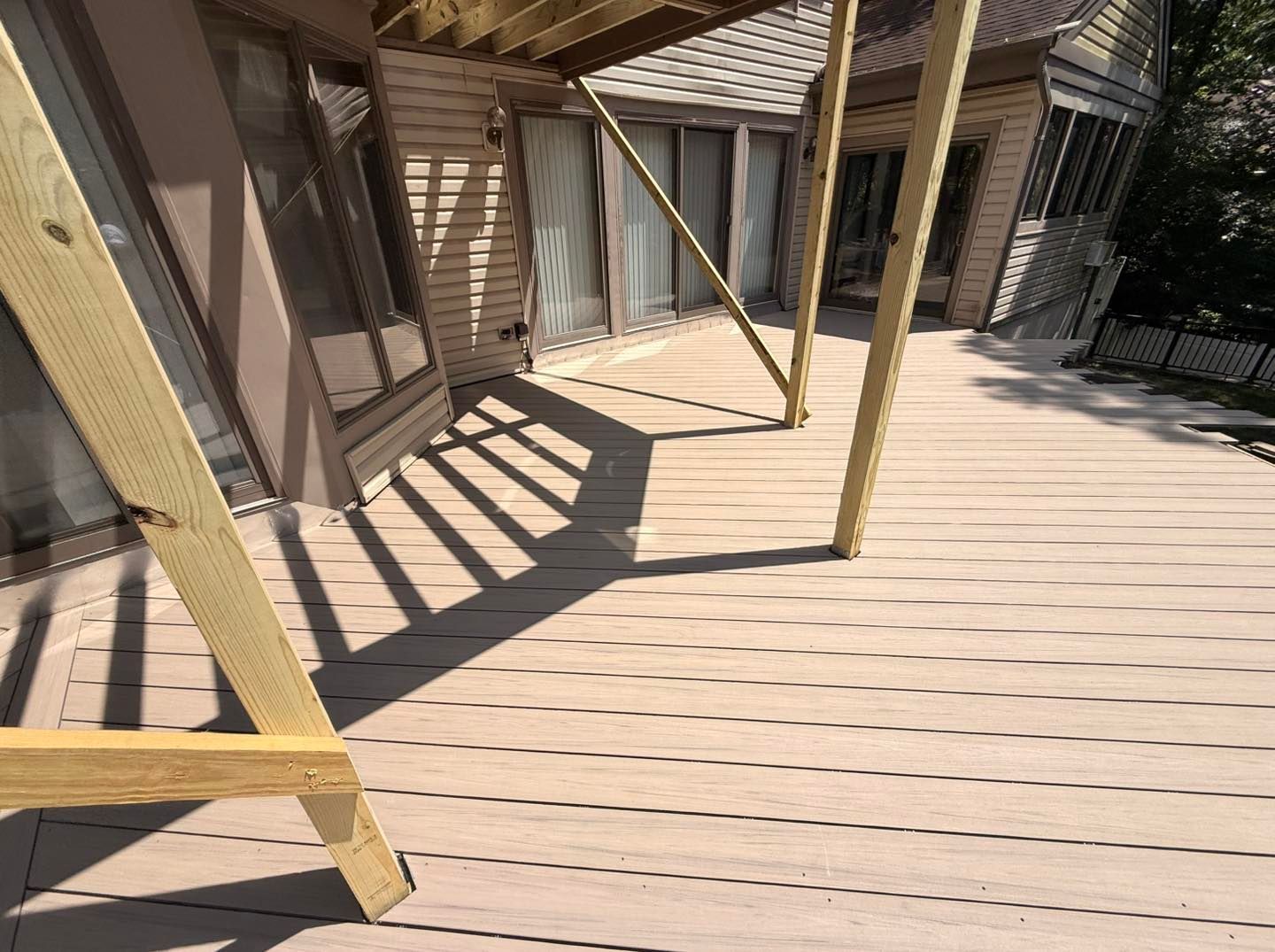 Deck with composite decking boards, supported by wooden posts, next to a house with windows and a door.