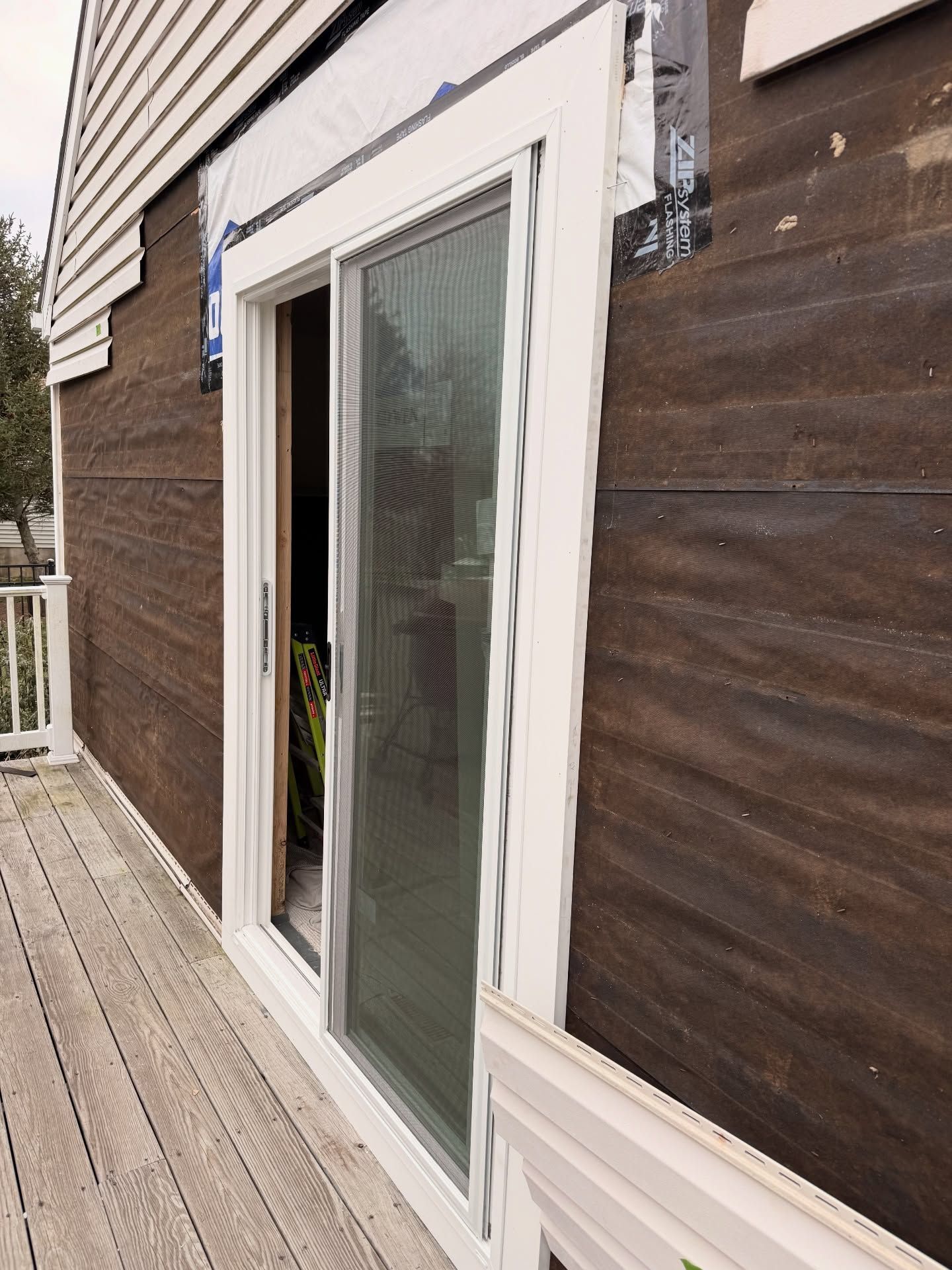 Exterior view of a sliding glass door being installed on a house with brown siding and a wooden deck.