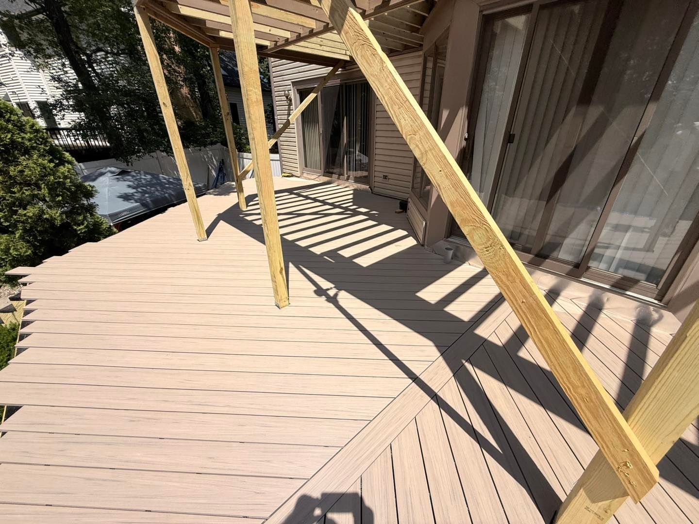 Wooden deck with pergola, casting shadows onto the deck. House with sliding glass doors visible.
