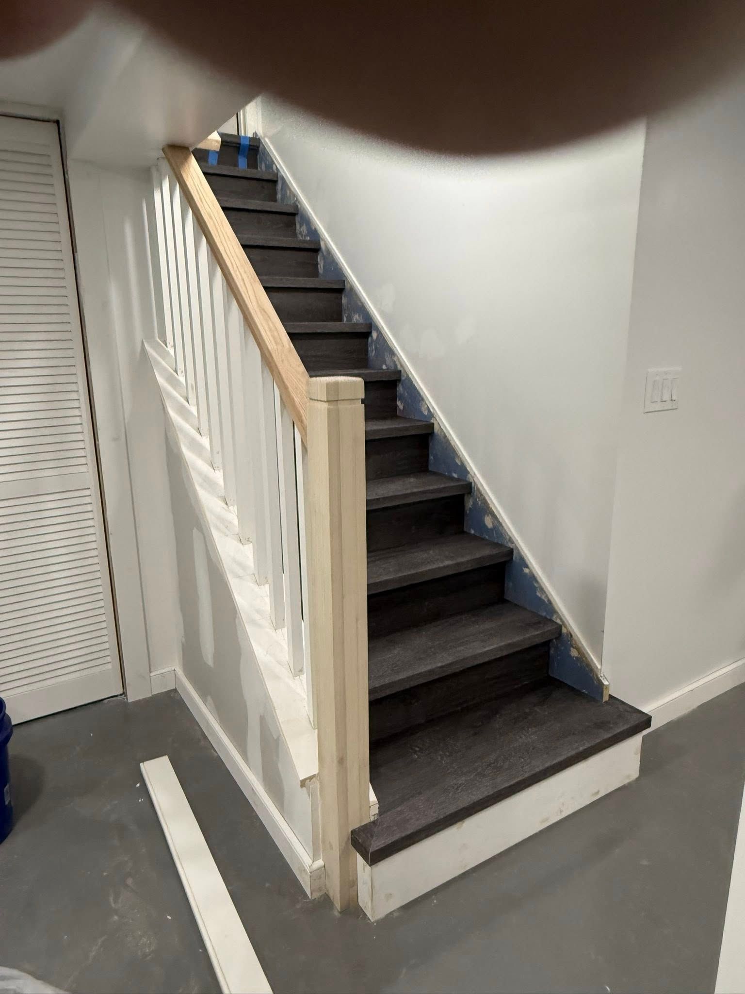 Staircase with gray treads, white risers and railing, light wood handrail, and white walls.