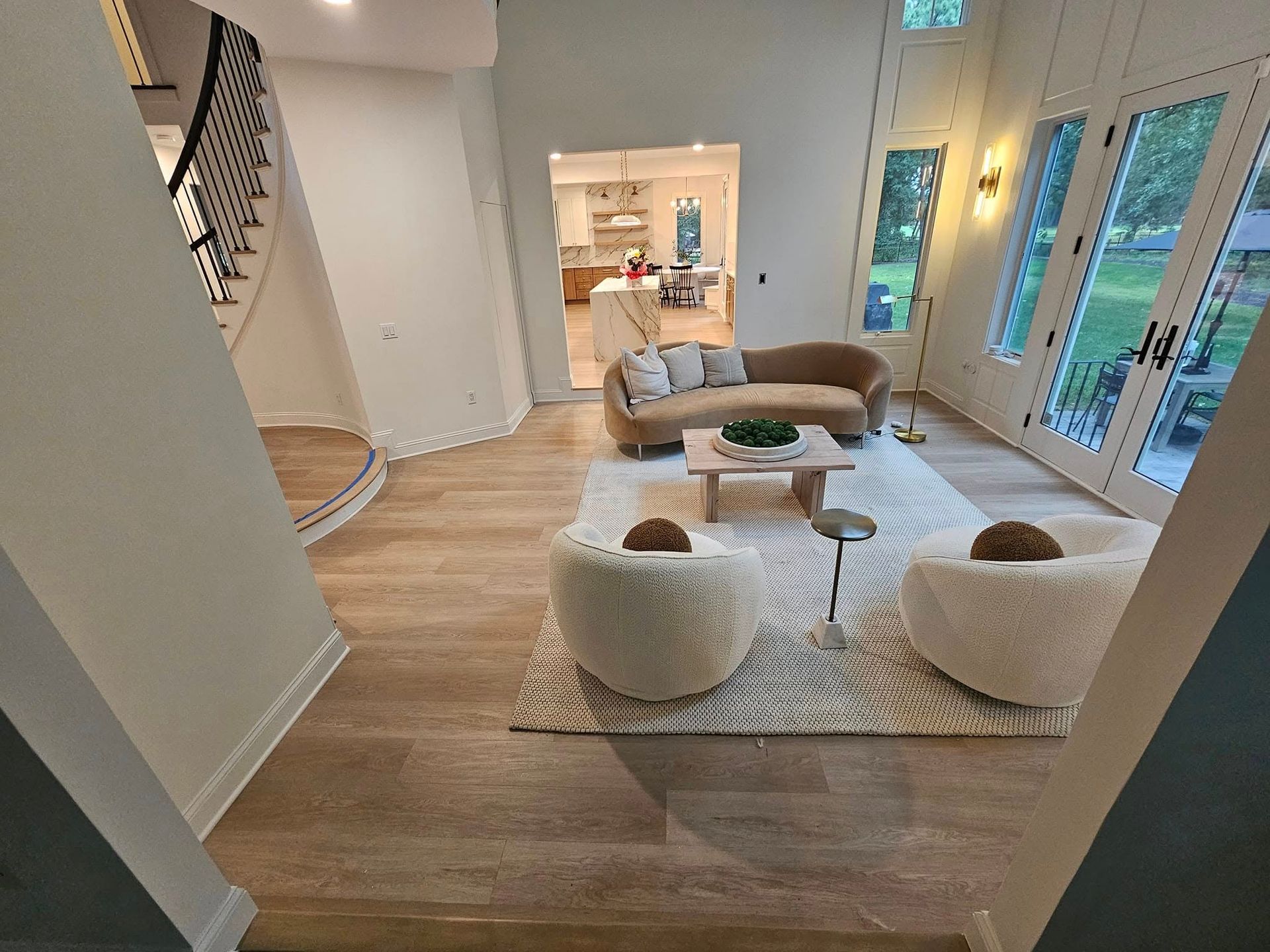 Living room with a sofa, two chairs, rug, and coffee table. Windows and a staircase are also visible.