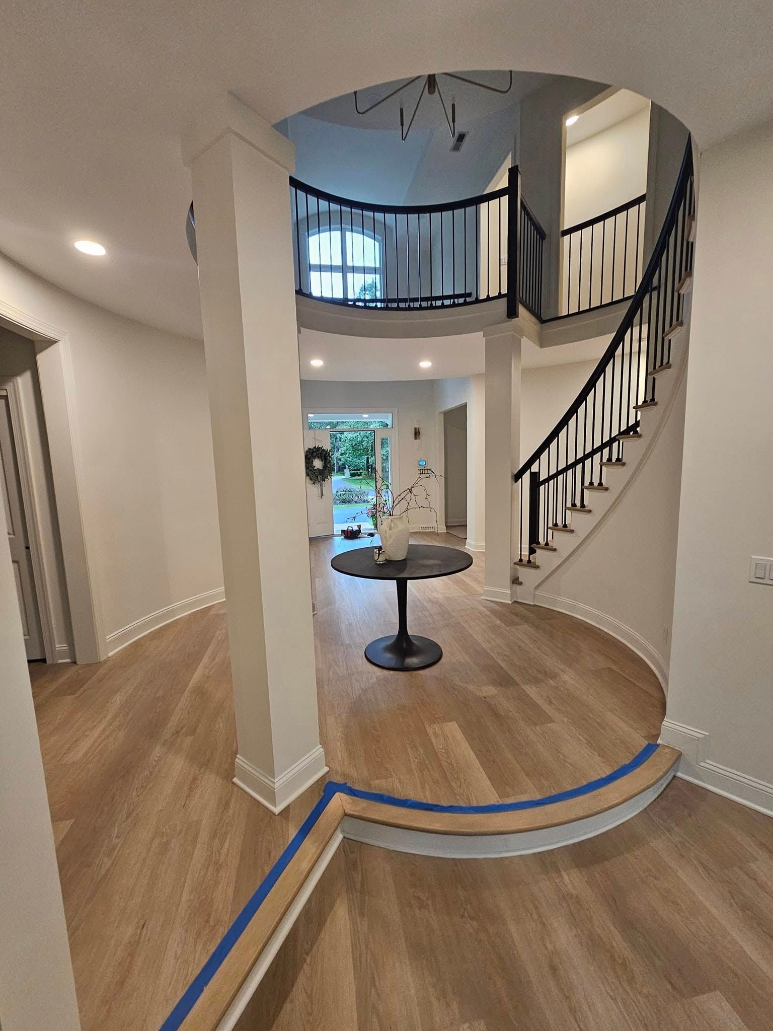 Foyer with hardwood floor, staircase, and round table. Archway leads to another room with greenery.