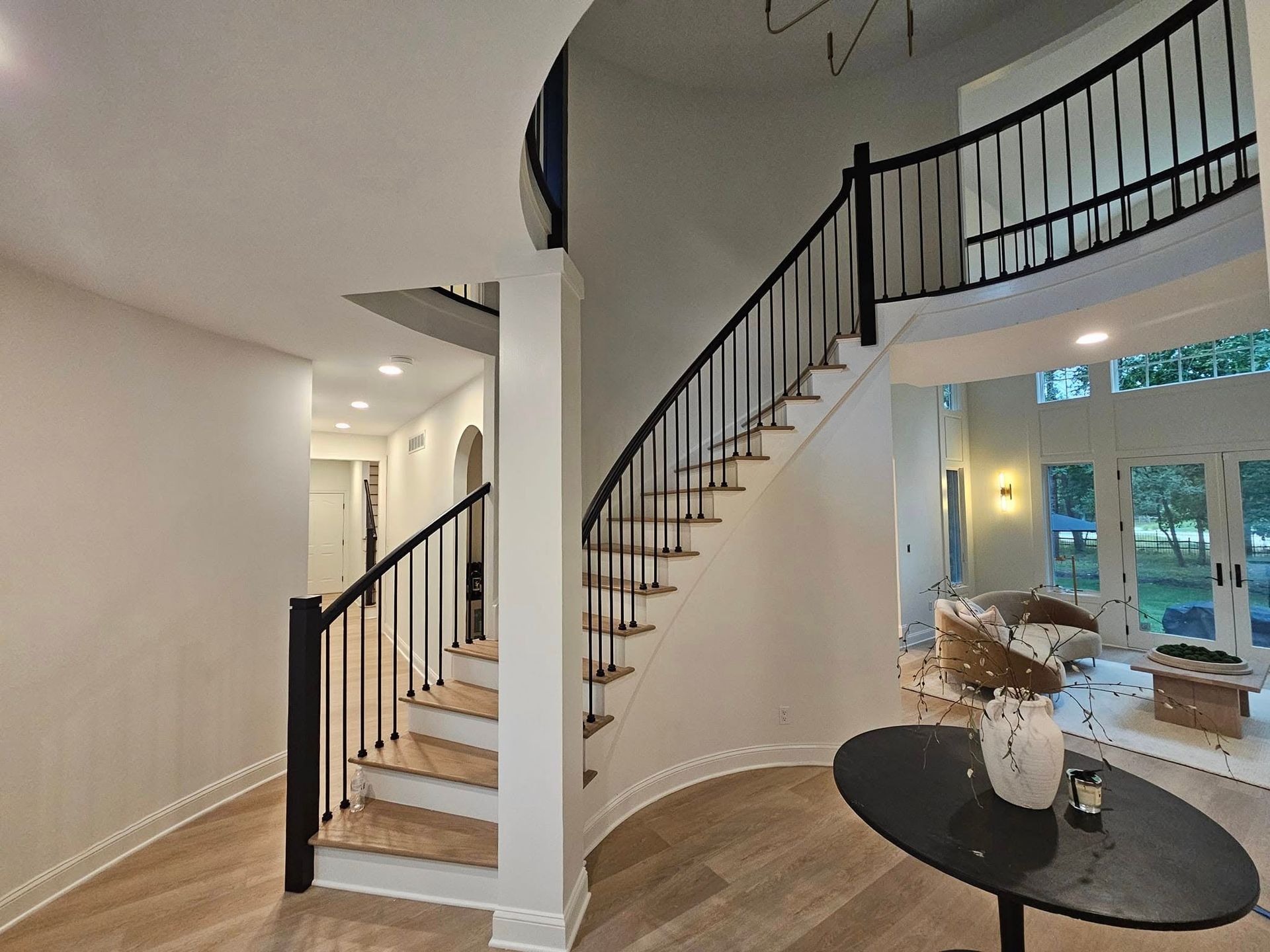 A curved staircase with black railing leads to an upper level, off a foyer with light wood floors.