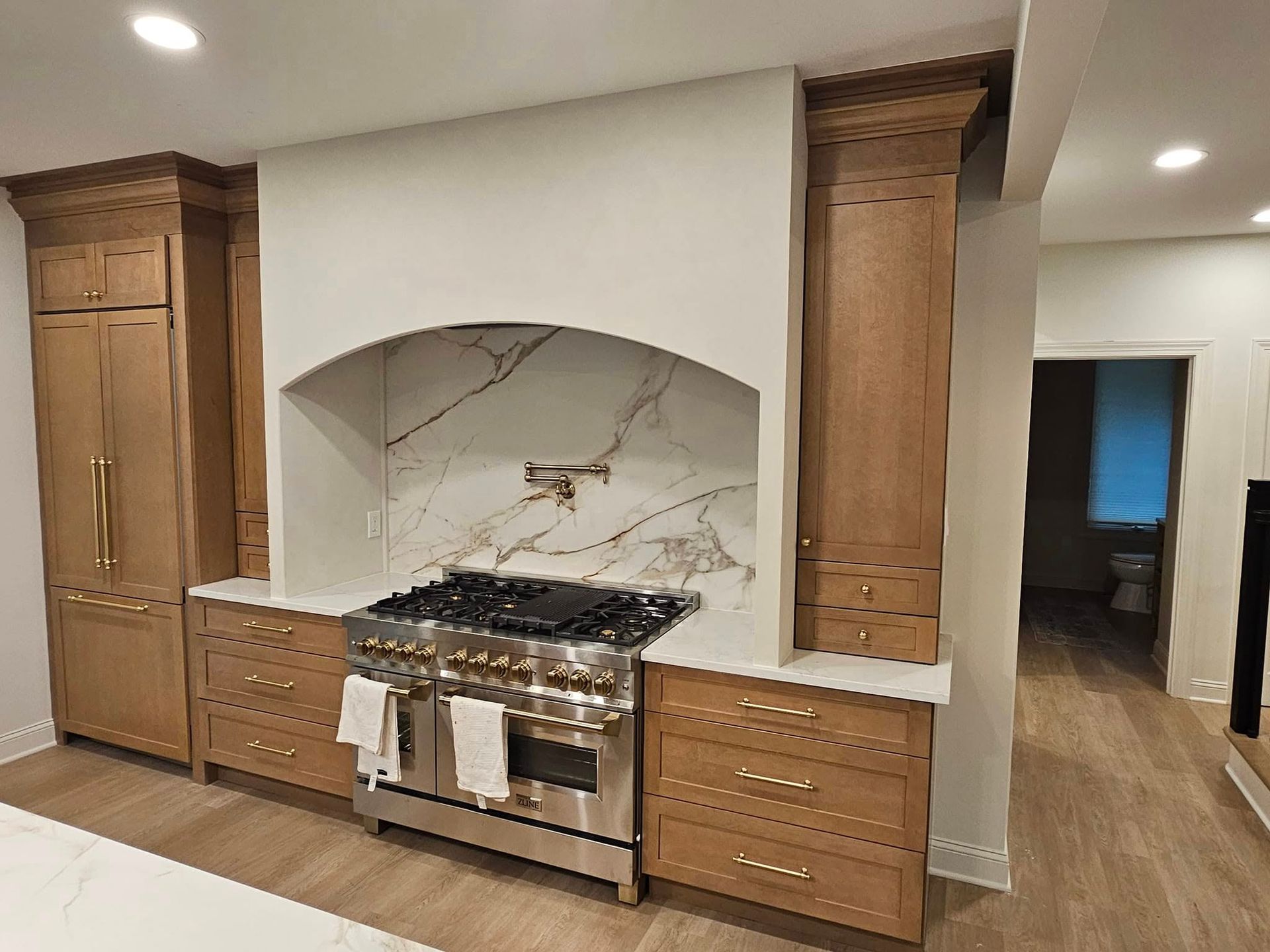 Kitchen with stainless steel range, marble backsplash, light wood cabinets, and white range hood.