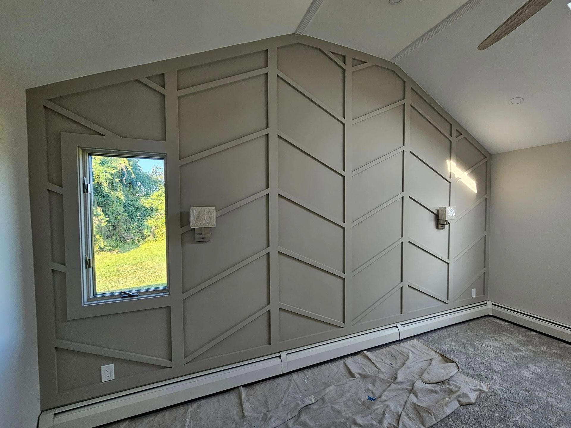 Gray wall with geometric wood paneling around a window and a sloped ceiling; unfinished room.