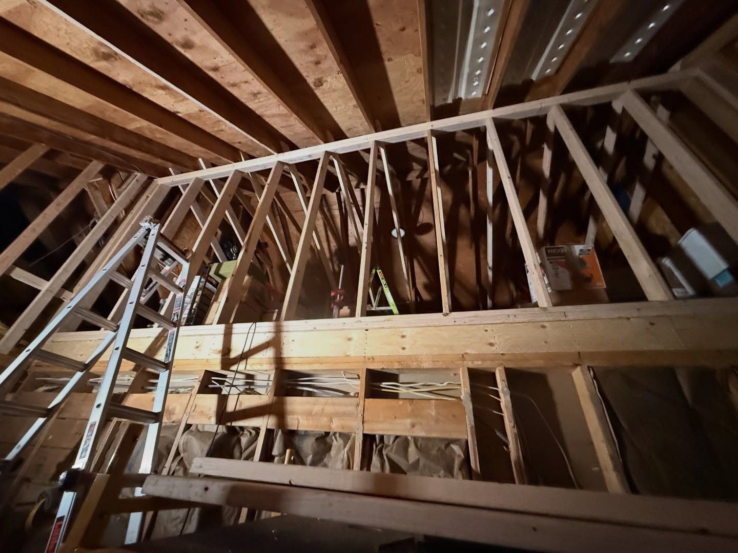Interior view of a wooden attic frame with a ladder. The structure shows unfinished construction.