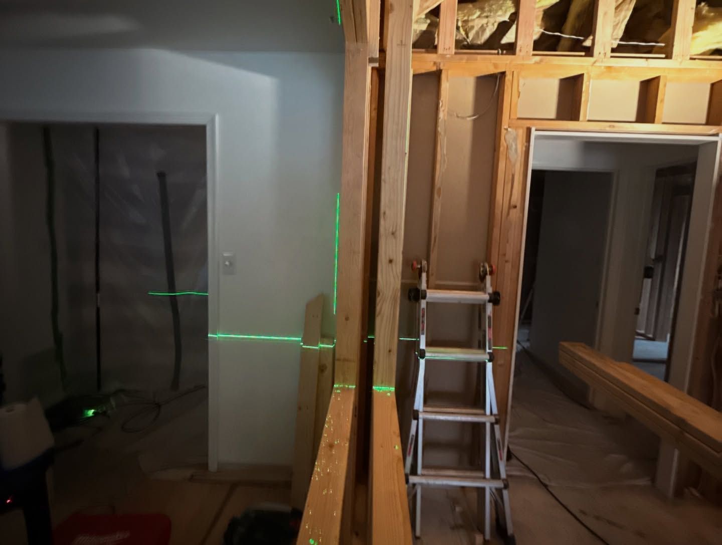 Interior renovation: wooden studs frame doorways, a green laser level projects lines.