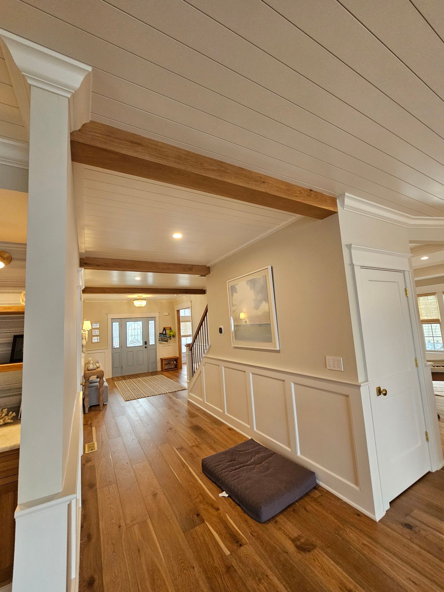 Interior view of a hallway with hardwood floors, white trim, and wooden beams. A painting hangs on the wall.