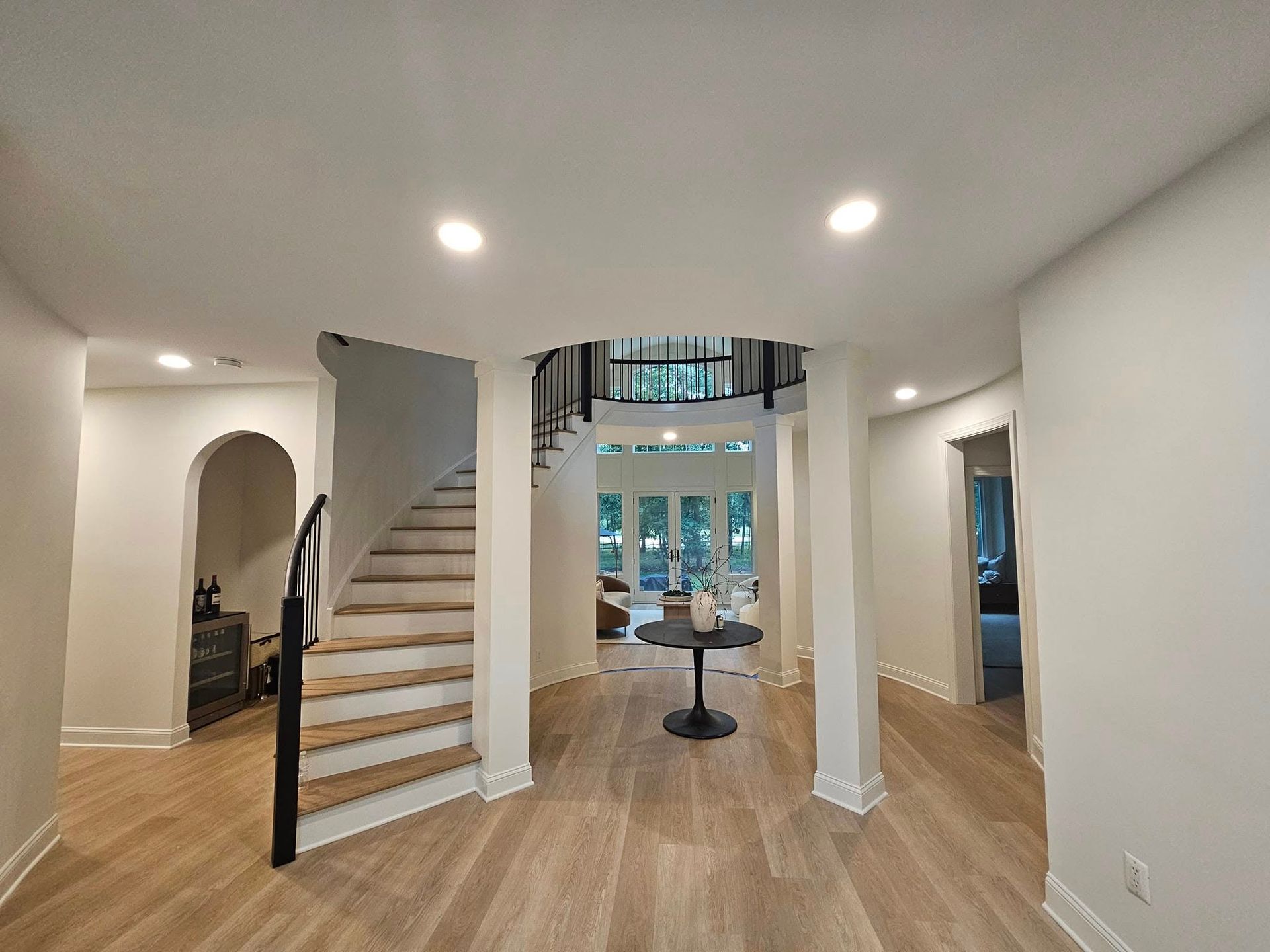Spacious entryway with curved staircase, light wood floors, and neutral walls; leads to an outdoor view.