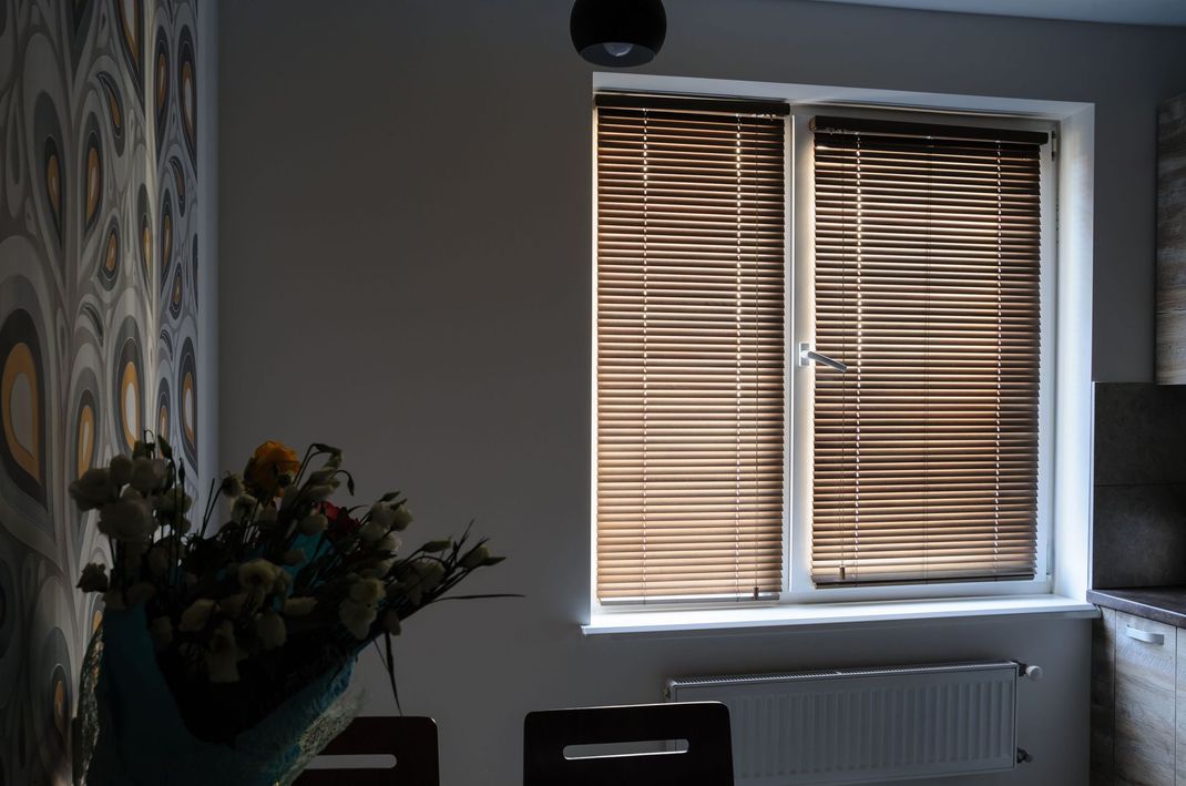 Dim room with patterned wall, flower vase, and a window with wooden blinds above a radiator.