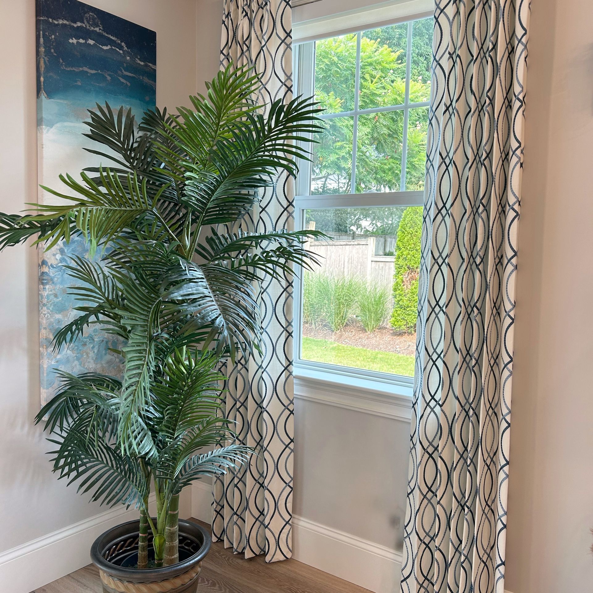 Potted palm beside a sunlit window with patterned curtains in a bright room