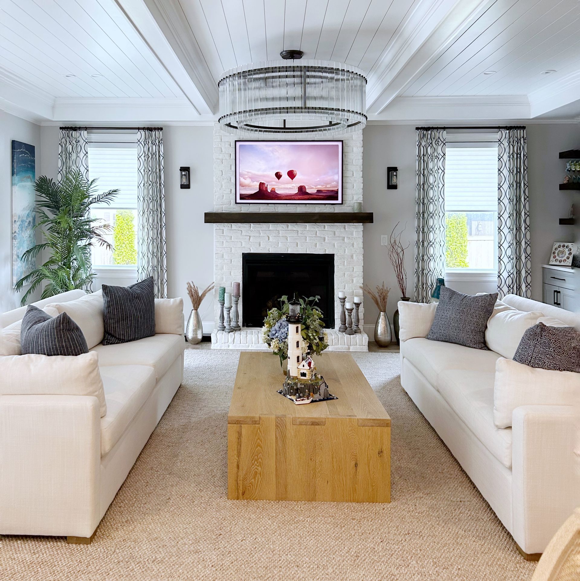 Bright living room with white sofas, wood coffee table, fireplace, and TV above the mantel