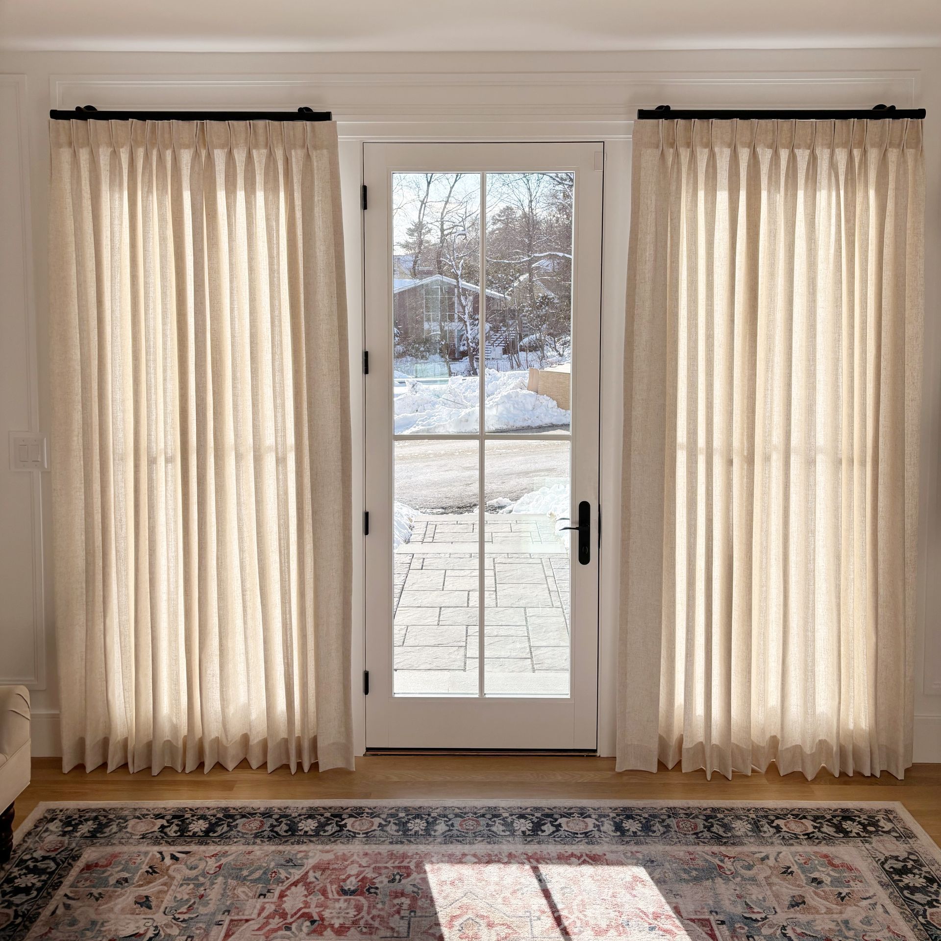 White French doors framed by cream curtains, with a snowy yard visible outside and a patterned rug inside.
