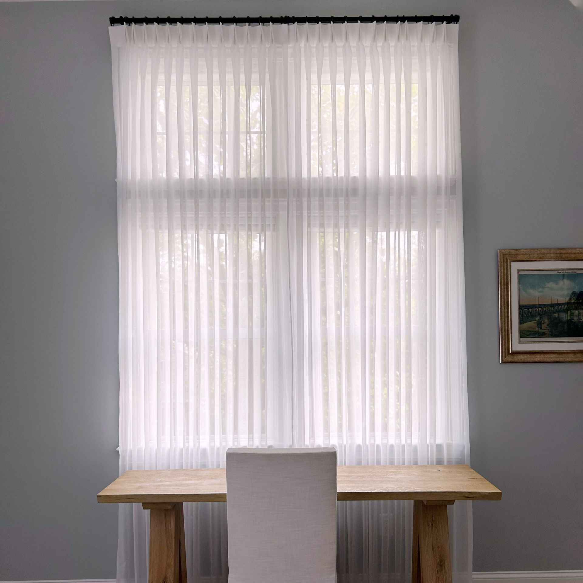 Minimal dining nook with wooden table, white chair, and sheer curtains over a window