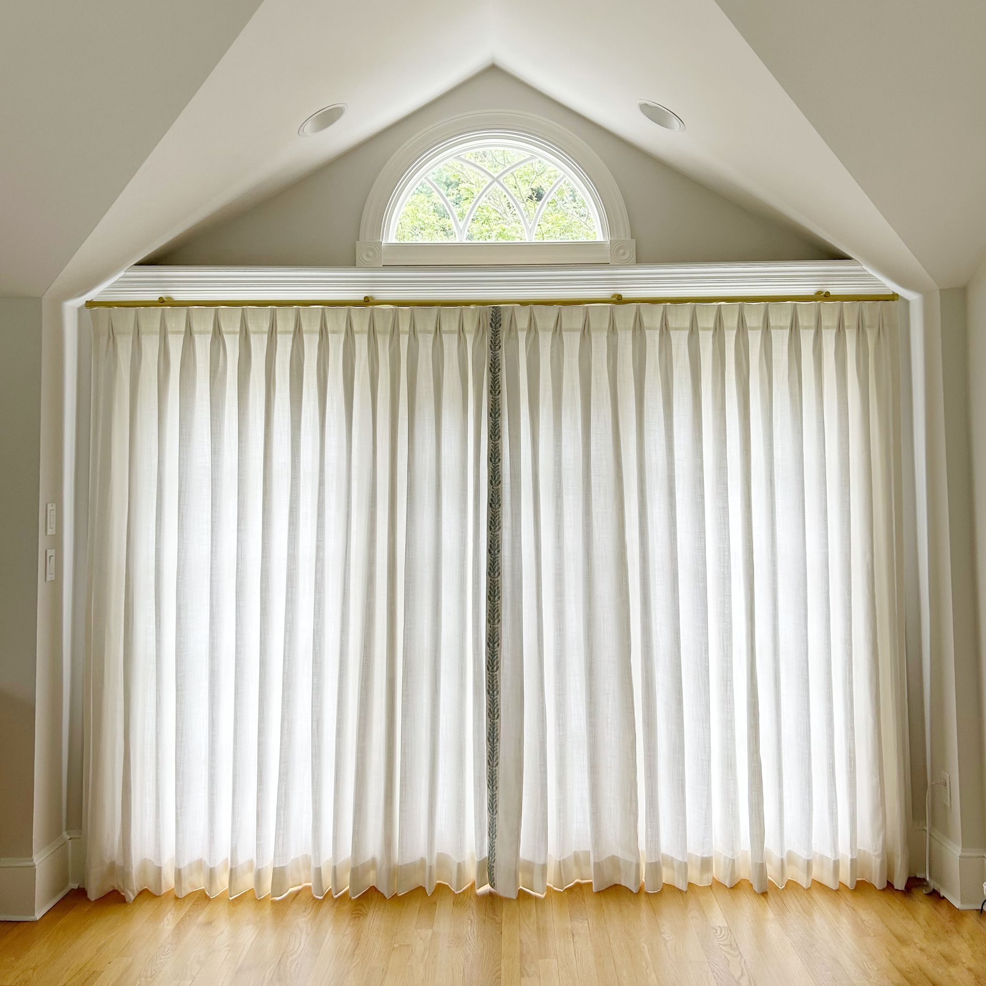 White sheer curtains covering a large arched window in a bright vaulted room