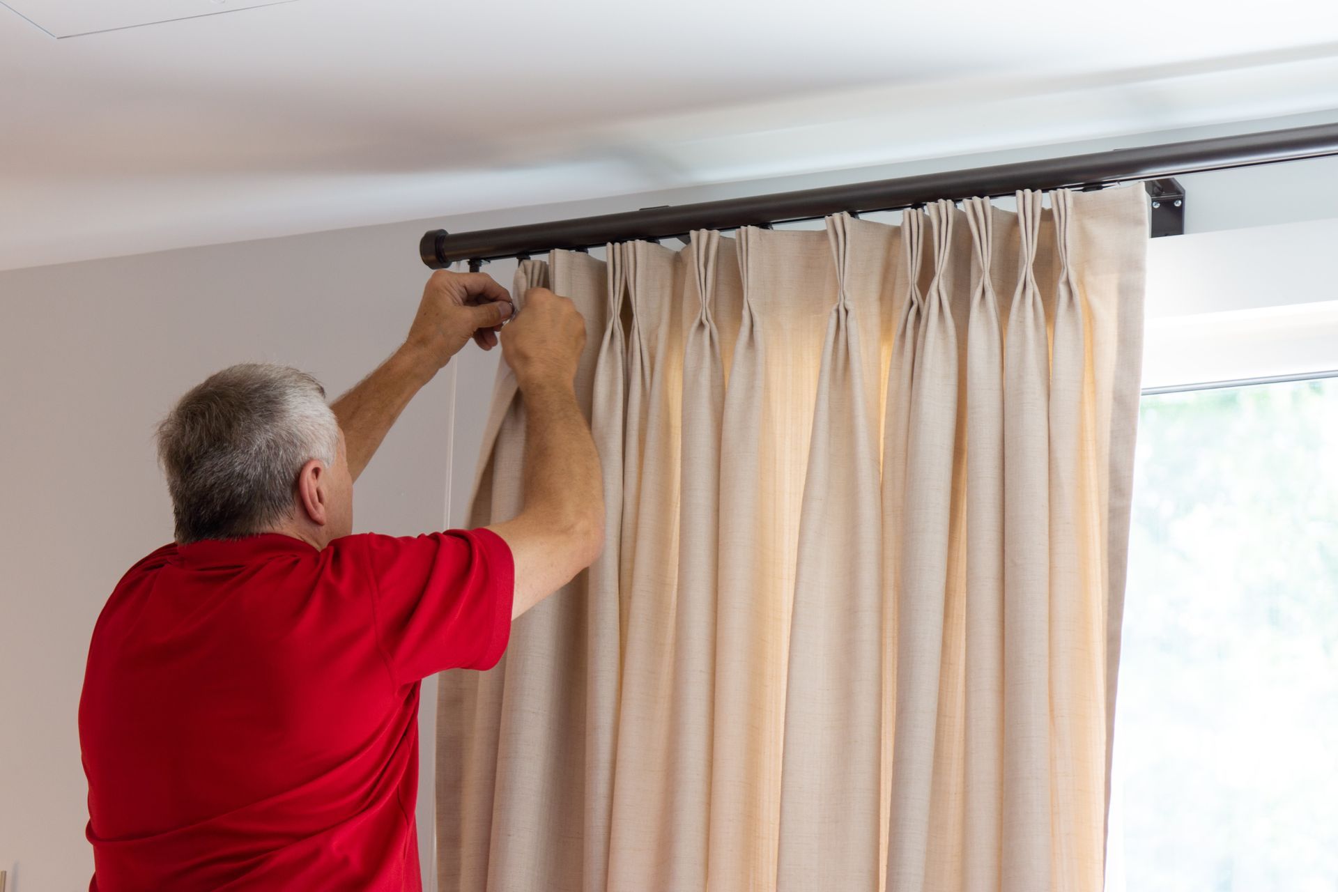 Person hanging beige curtains on a window rod indoors