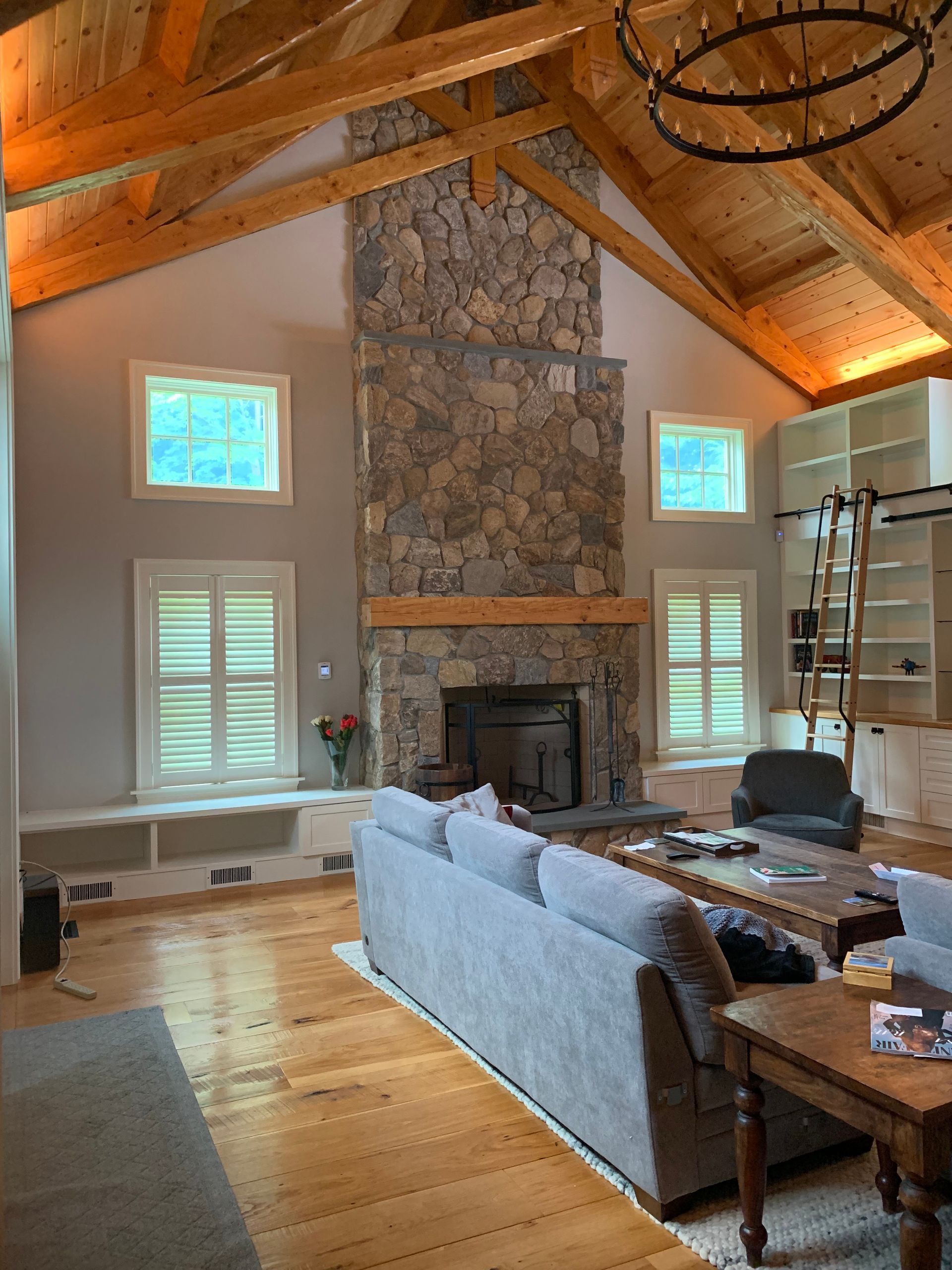 Cozy living room with stone fireplace, vaulted wood ceiling, gray sofa, and large windows