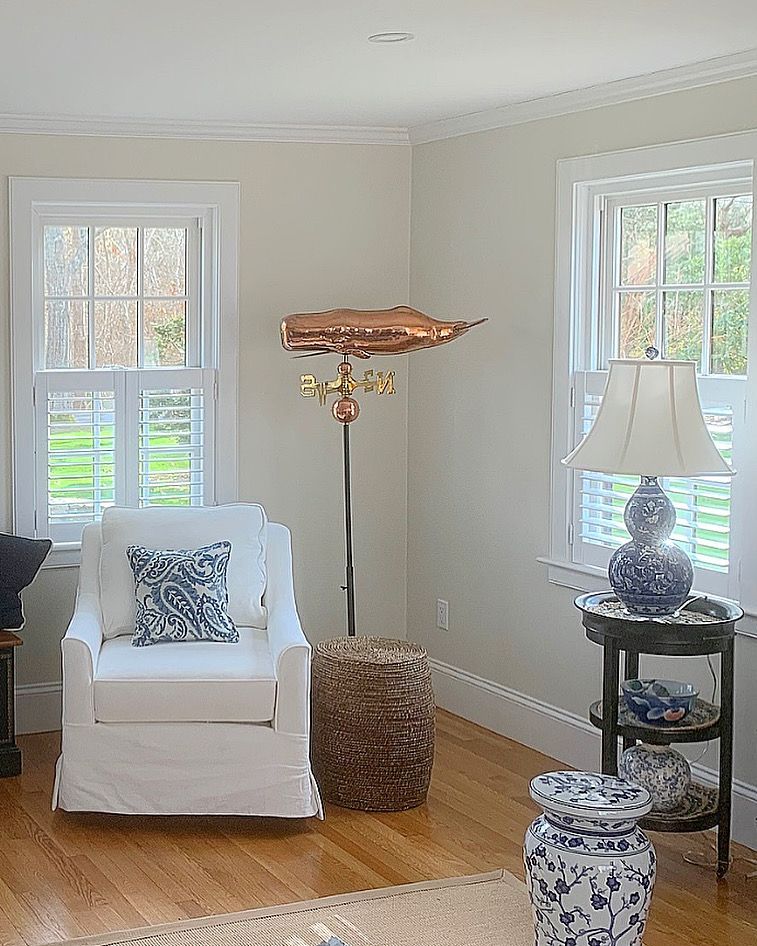 Bright living room with white armchair, floor lamp, side table, and sunlit windows.