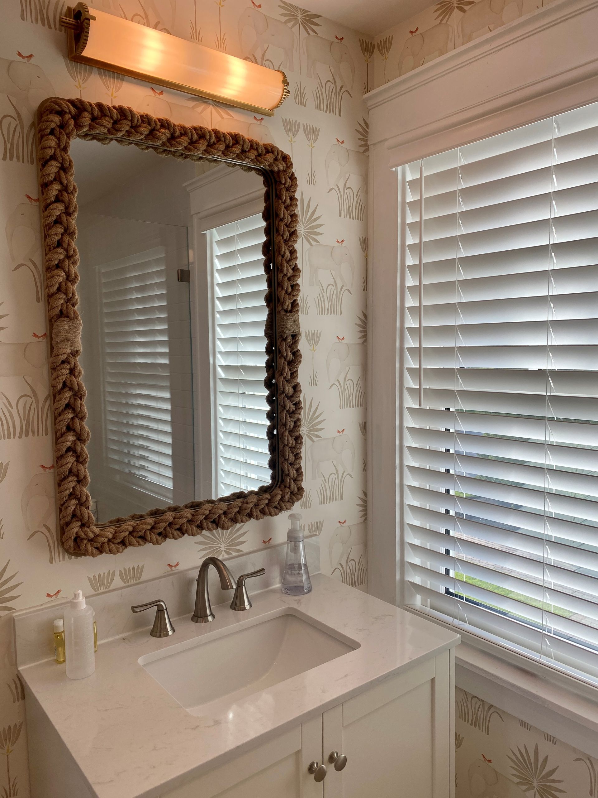 Small bathroom vanity with ornate mirror, wall light, white sink, and window blinds.