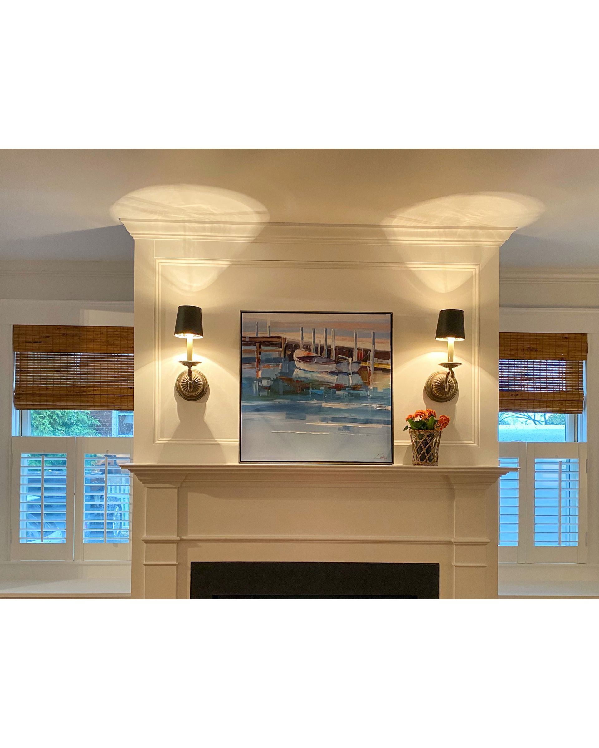 Decorative fireplace mantel with wall art, sconces, and blue window shutters in a bright room