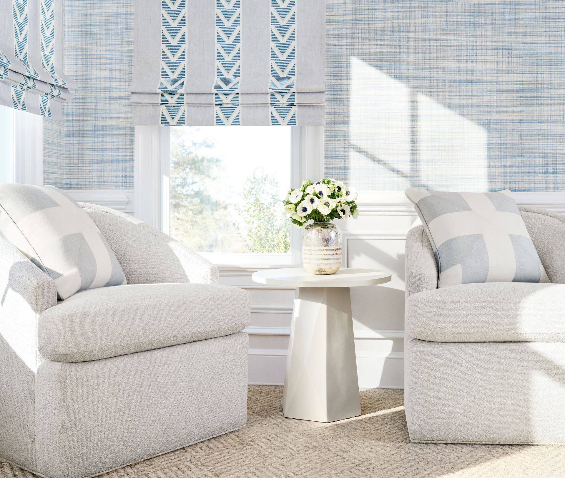 Bright, airy living room with white armchairs, patterned curtains, and a small table with flowers.