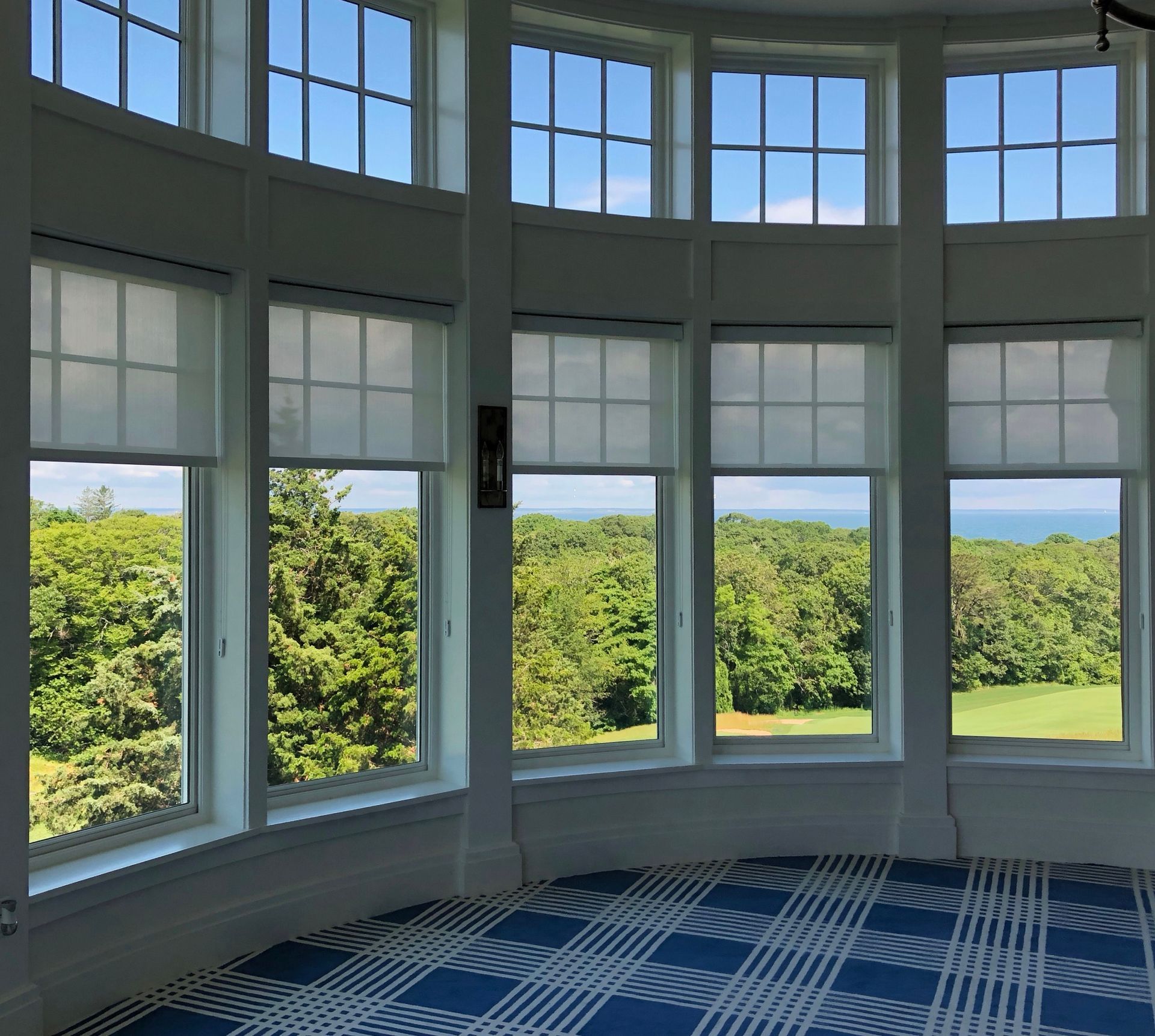 Curved room with tall windows overlooking green trees and blue water, with a blue patterned carpet.