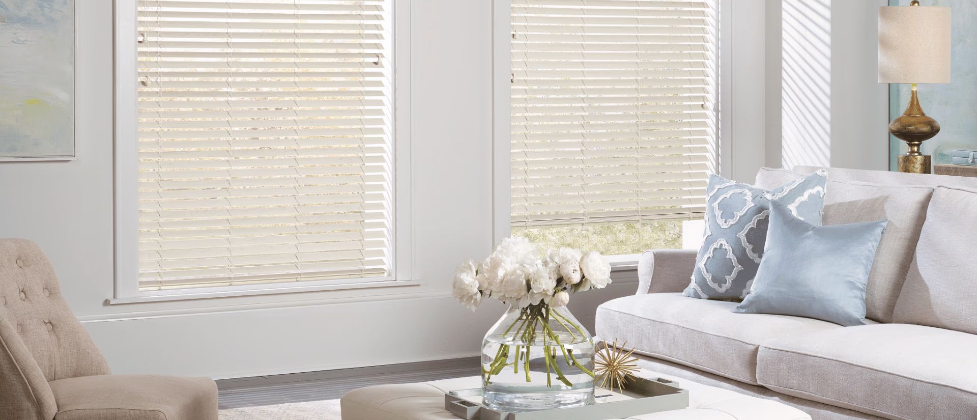 Bright living room with gray sofa, white flowers on coffee table, and sunlight through blinds
