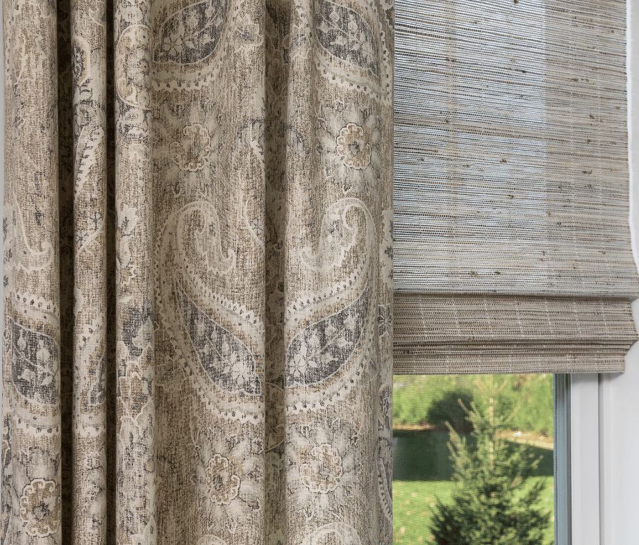 Patterned curtains beside a window with a woven blind, showing a view of green grass outside