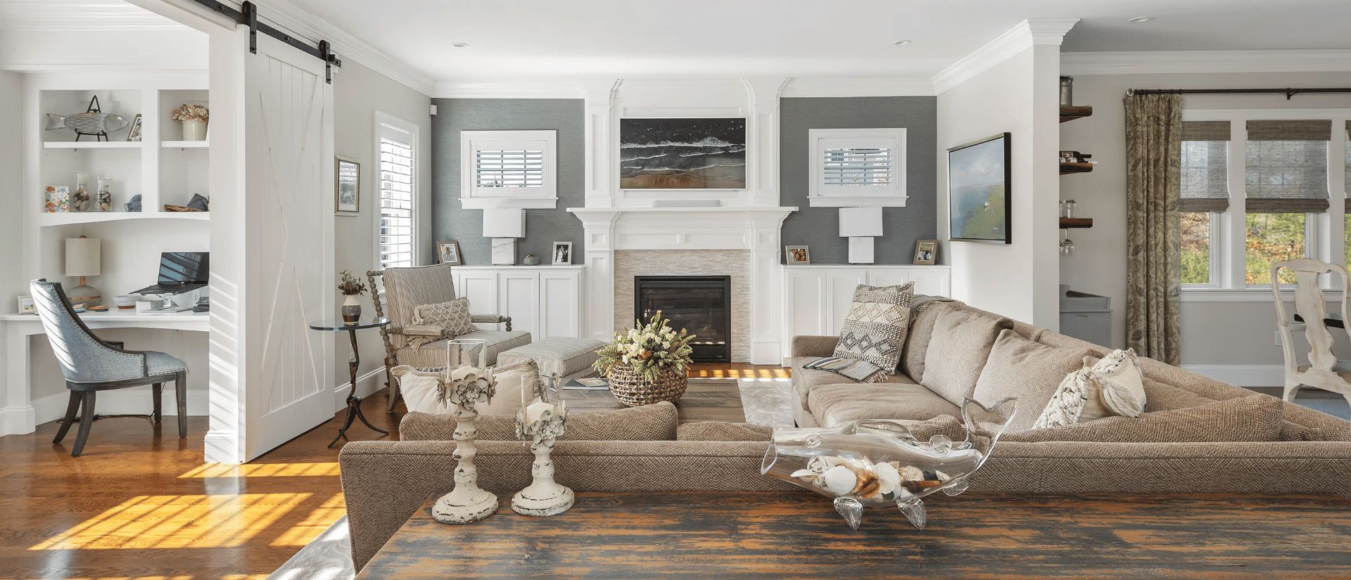 Bright, elegant living room with a fireplace, patterned sofa, white built-ins, and hardwood floors