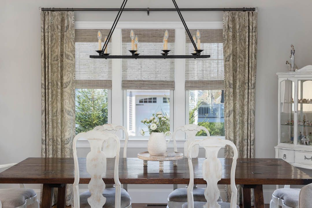 Dining room with a dark wood table, white chairs, large window, and black chandelier.