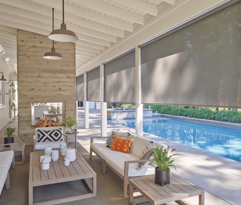 Covered patio with sofa, coffee table, and pool view through rolled shades