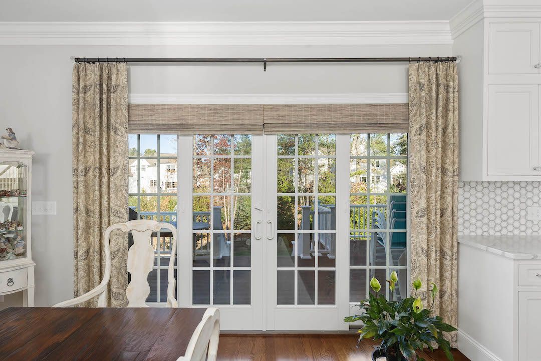 Bright dining room with French doors, beige curtains, white walls, and a view of the garden outside