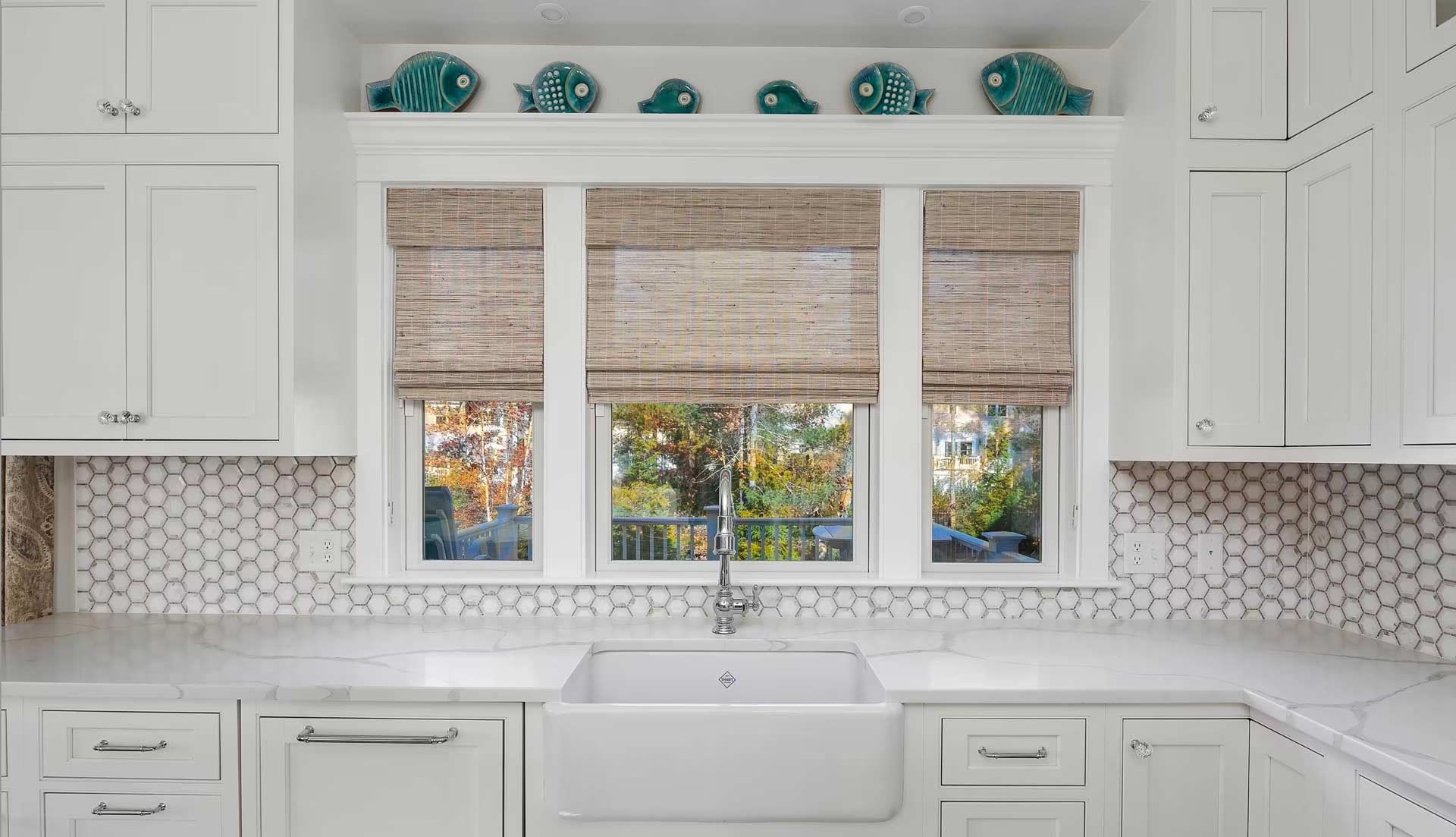 Bright white kitchen with farmhouse sink, patterned backsplash, and window with woven blinds