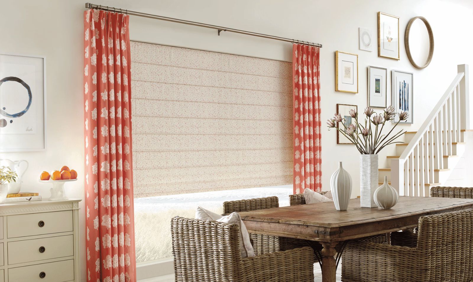 Bright dining room with woven chairs, wood table, red curtains, and a staircase on the right.