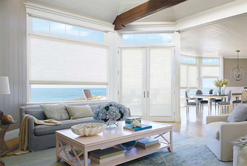 Bright airy living room with white sofas, wooden coffee table, blue accents, and large windows