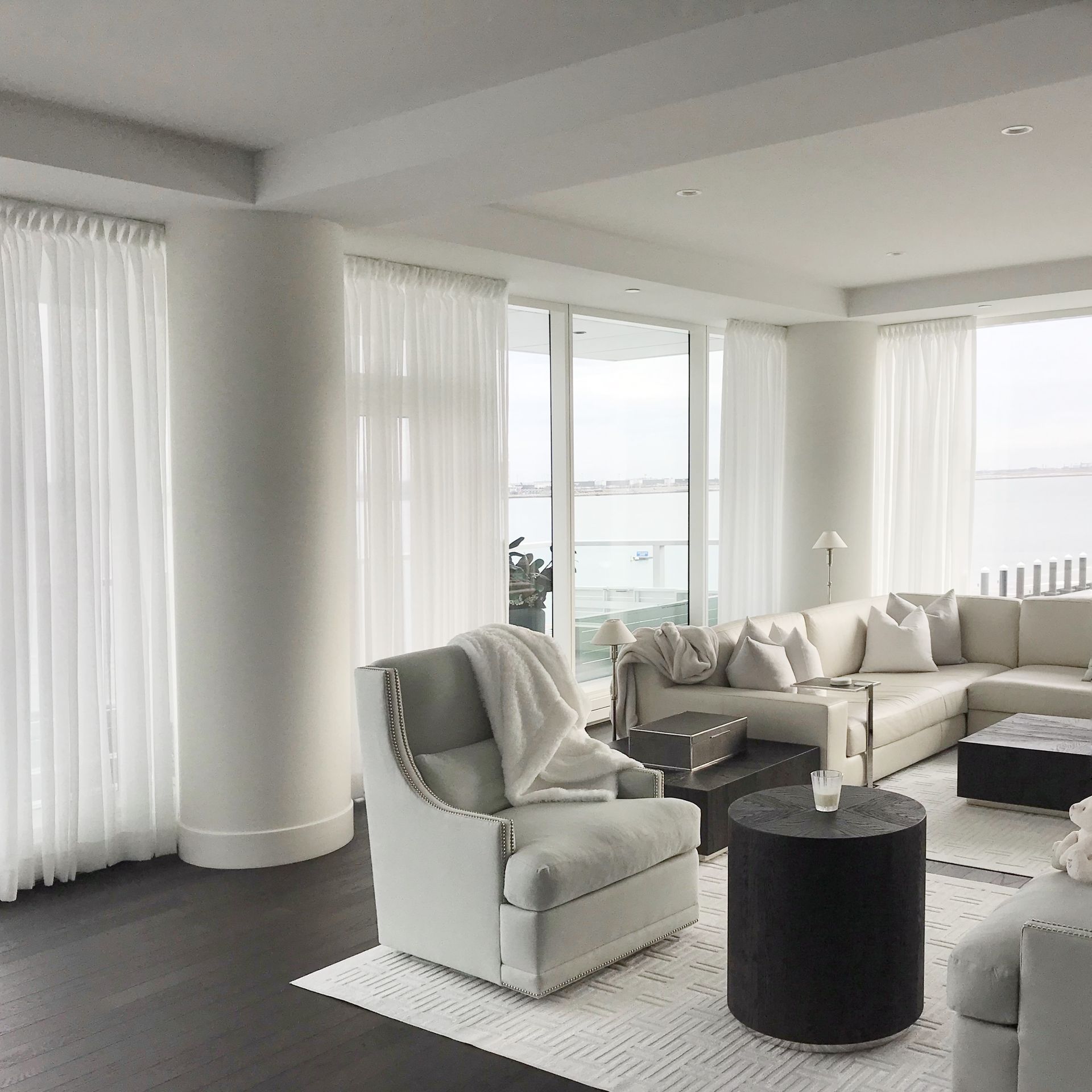 Bright modern living room with white sofas, large windows, and dark wood floors