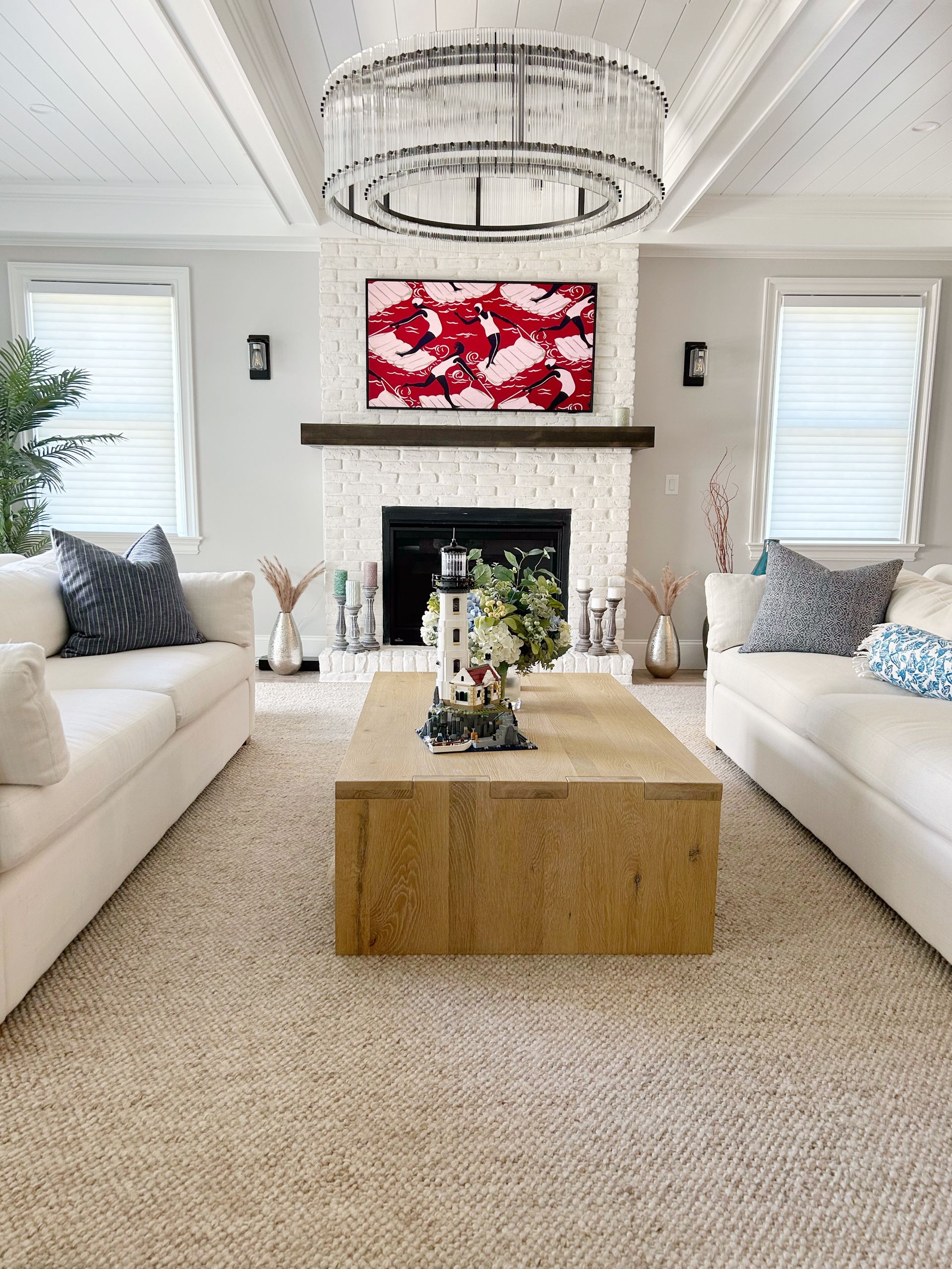 Bright living room with white sofas, marble fireplace, red abstract art, and a wooden coffee table