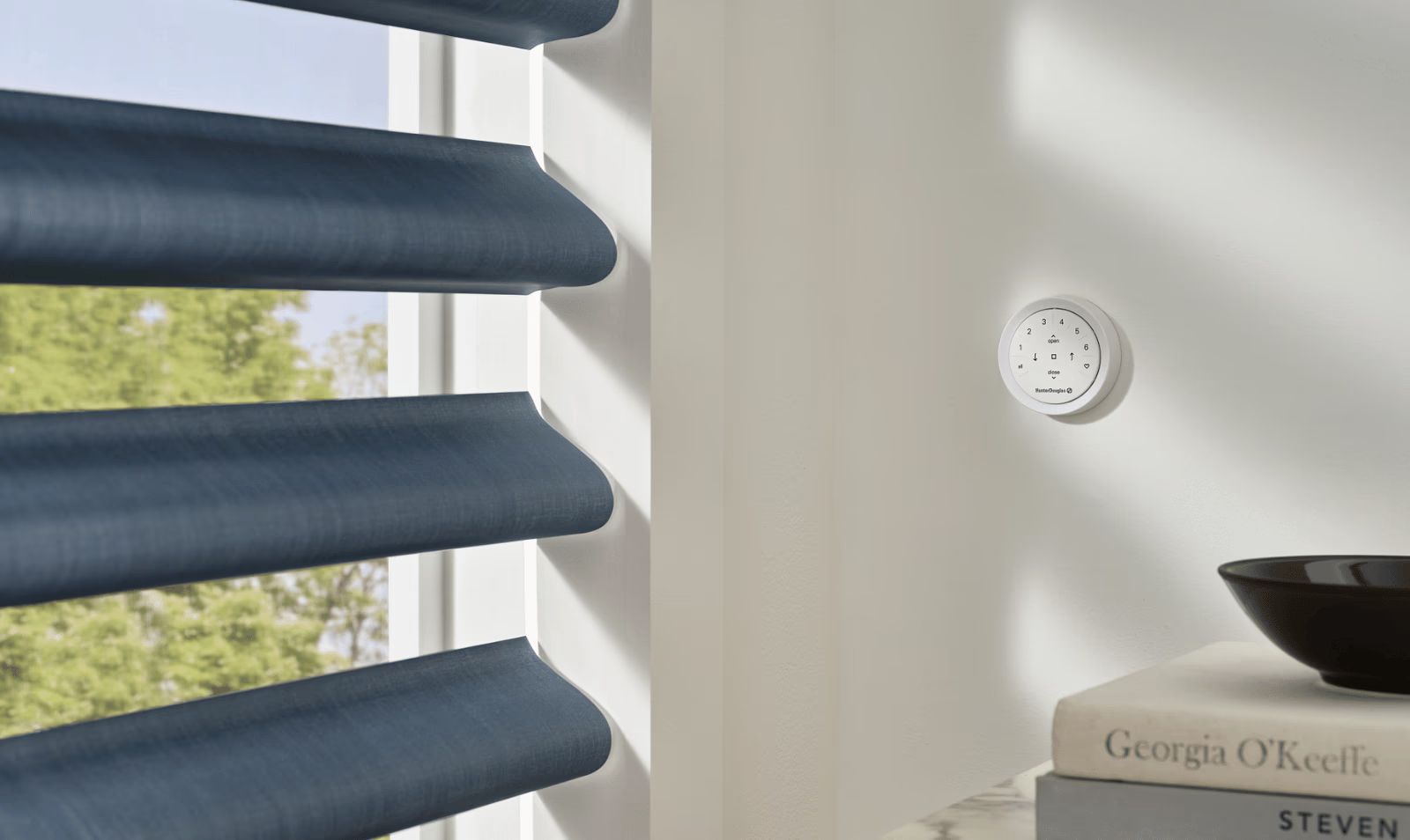 Blue window blinds beside a bright wall with a small round white device and a dark bowl on a table