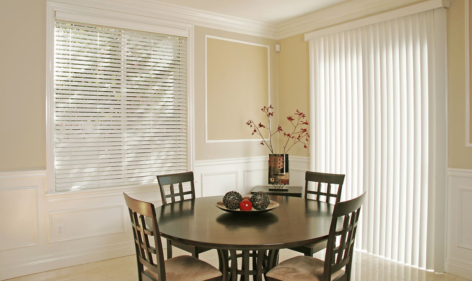 Dining room with round table, four chairs, white blinds, and soft beige walls.