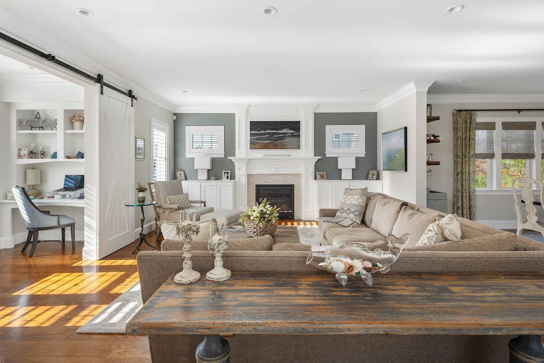 Bright living room with a fireplace, light walls, white furniture, and a wooden coffee table with decor.