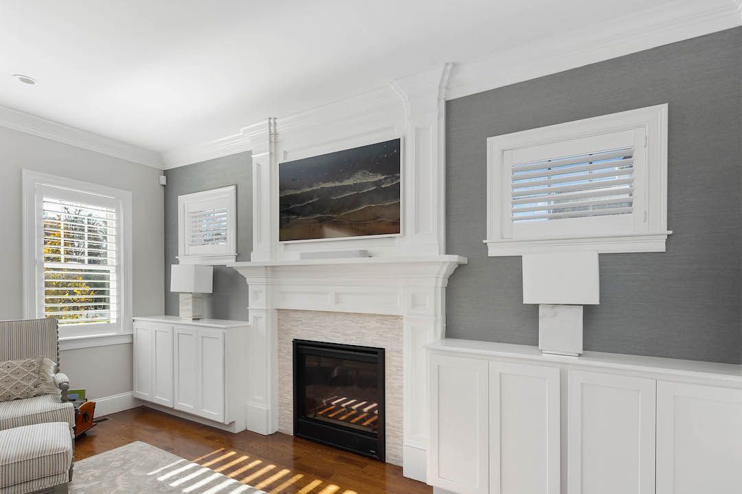Bright living room with gray walls, white wainscoting, and a white fireplace with a framed landscape above.