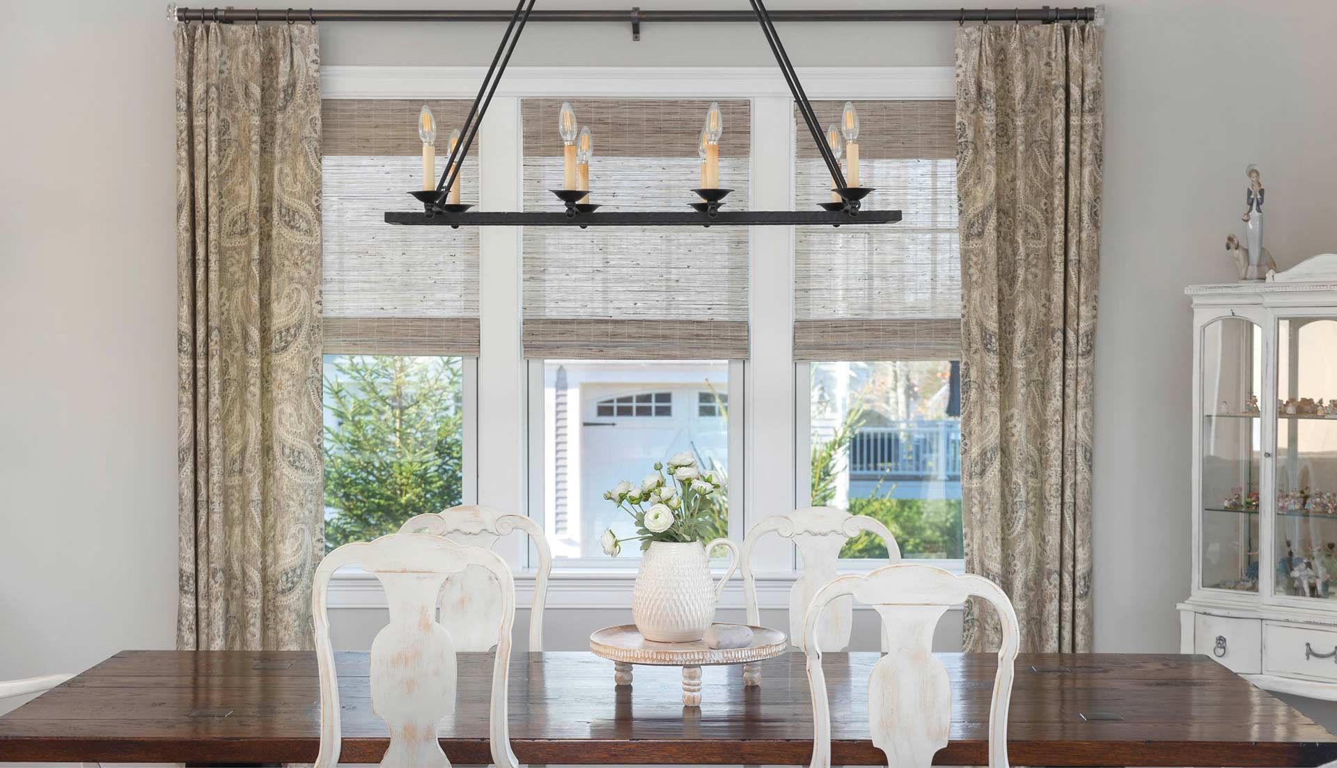 Bright dining room with white chairs, dark table, large window, and black chandelier across the center.