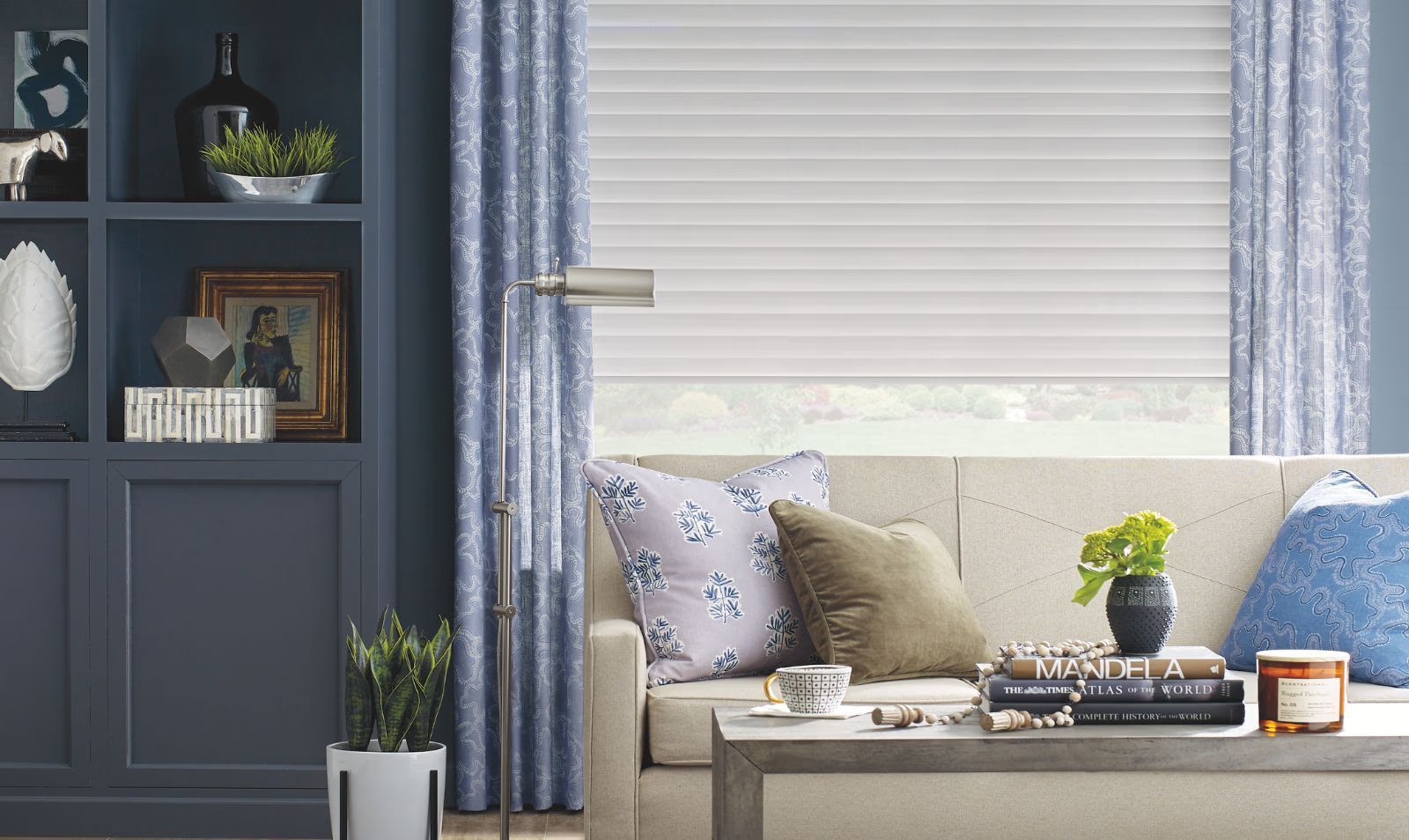 Cozy living room with blue walls, window blinds, curtains, a sofa, and a coffee table with plants and decor