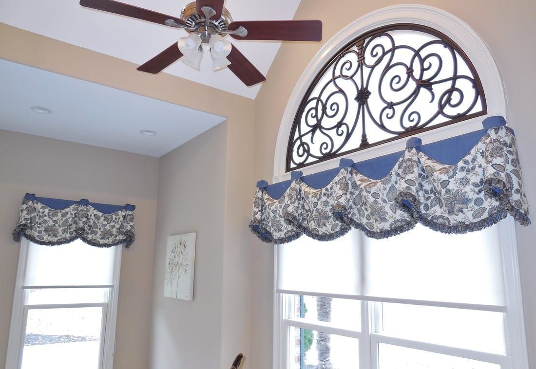 Interior with tall windows, blue scalloped valances, decorative iron arch, and a ceiling fan in a beige room