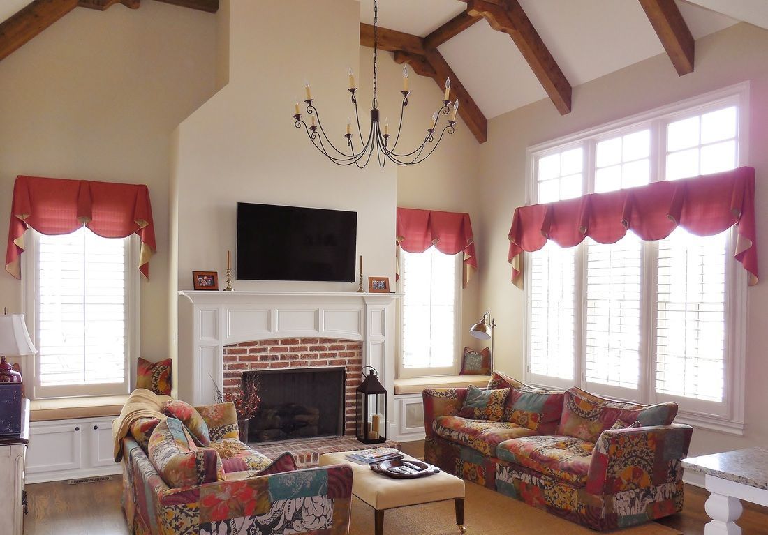 Bright living room with fireplace, TV, patterned sofas, red valances, and vaulted ceiling with chandelier