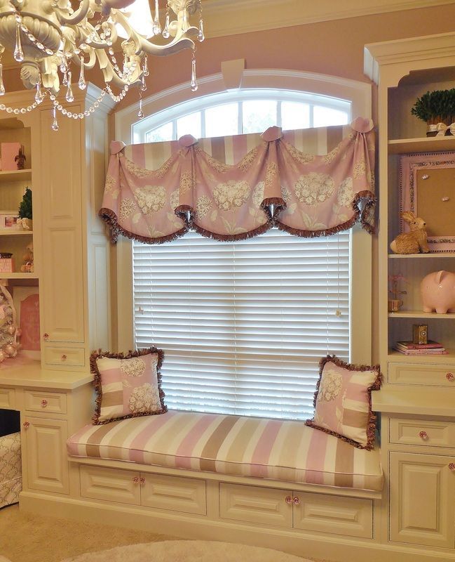 Elegant window seat with pink striped cushion, decorative valance, and built-in shelves in a cream room
