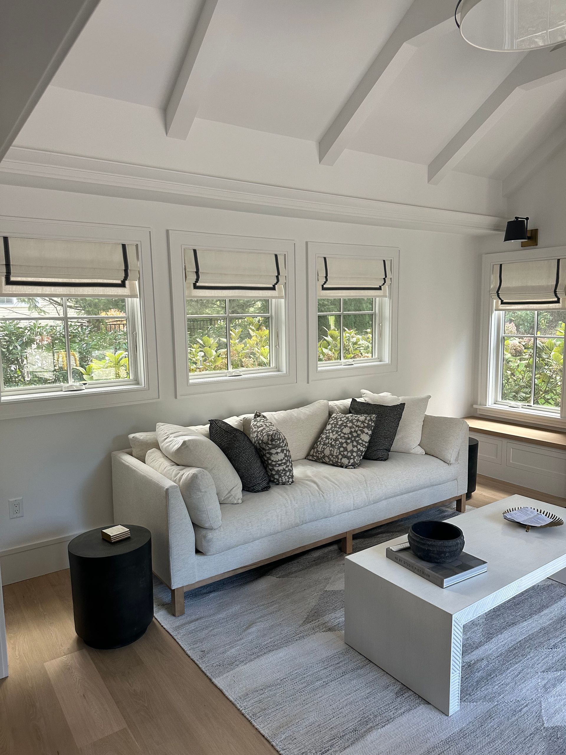 Bright living room with white sofa, coffee table, and multiple windows under a vaulted ceiling
